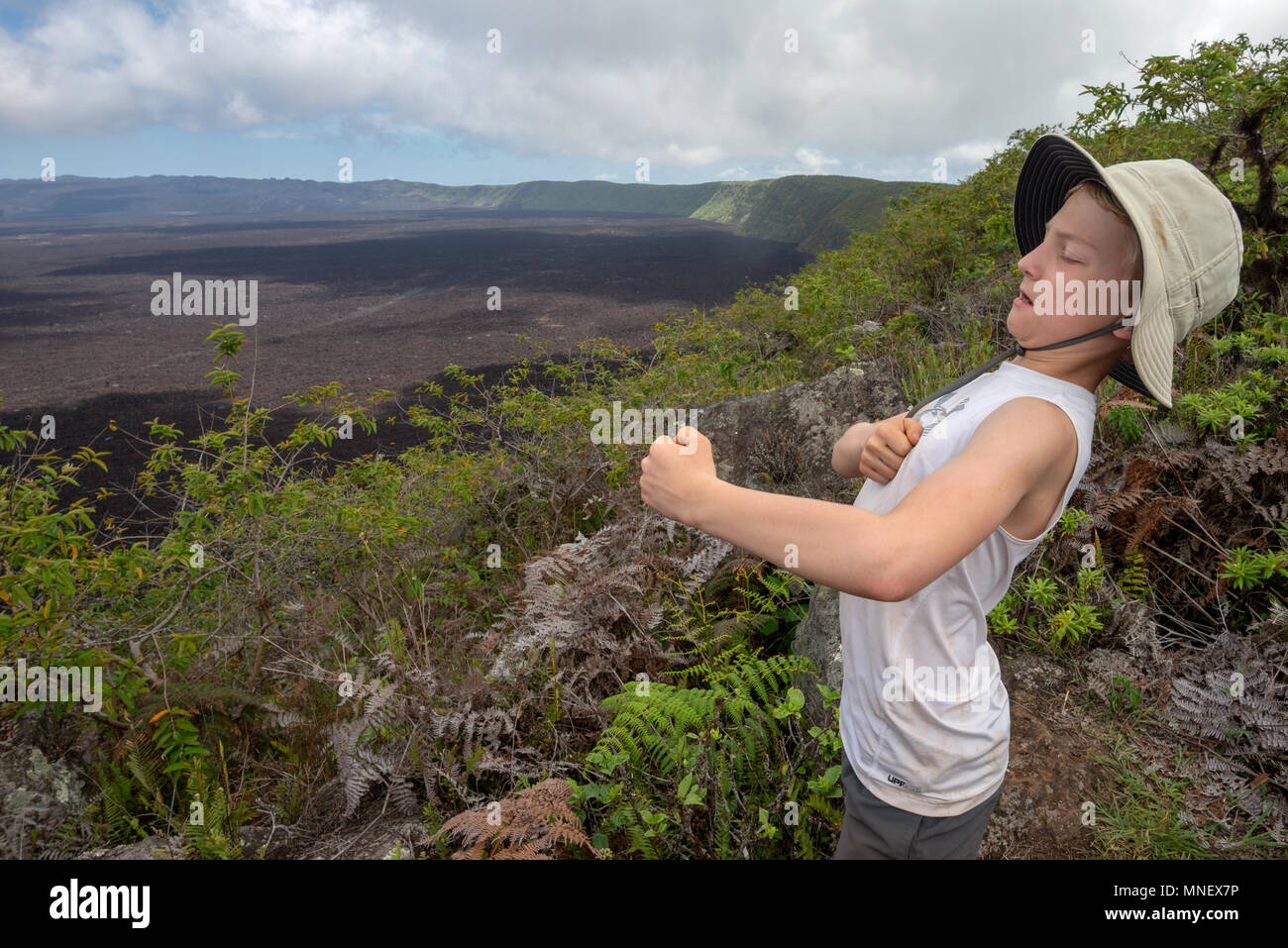 Ragazzo scherzosamente battendo il suo petto sul bordo del vulcano Sierra Negra, Isole Galapagos, Ecuador. Foto Stock