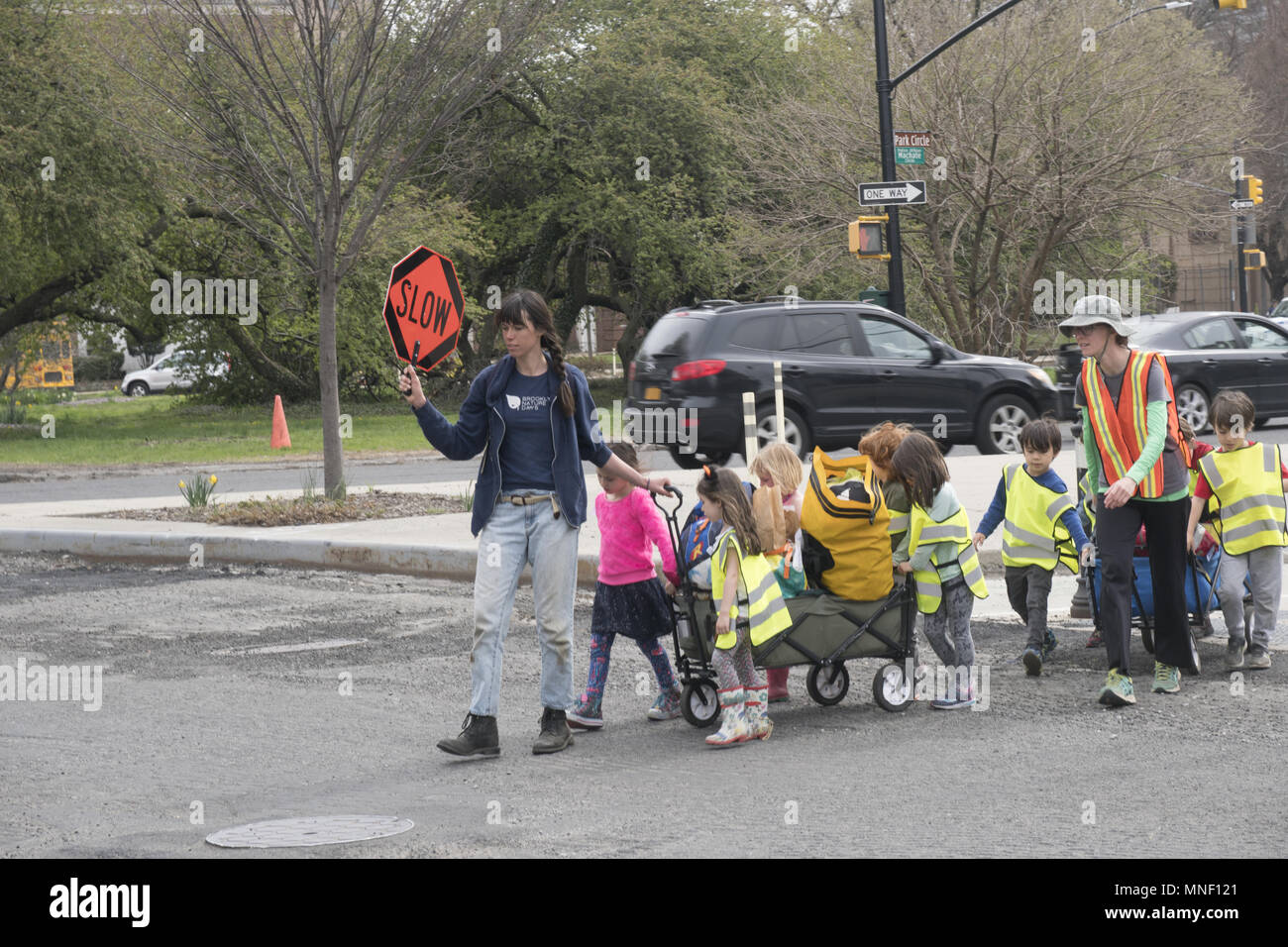 Insegnante con segno di traffico in passeggiate a mano una classe di giovani i bambini attraverso un grande incrocio sul loro modo di Prospect Park a Brooklyn, New York. Foto Stock