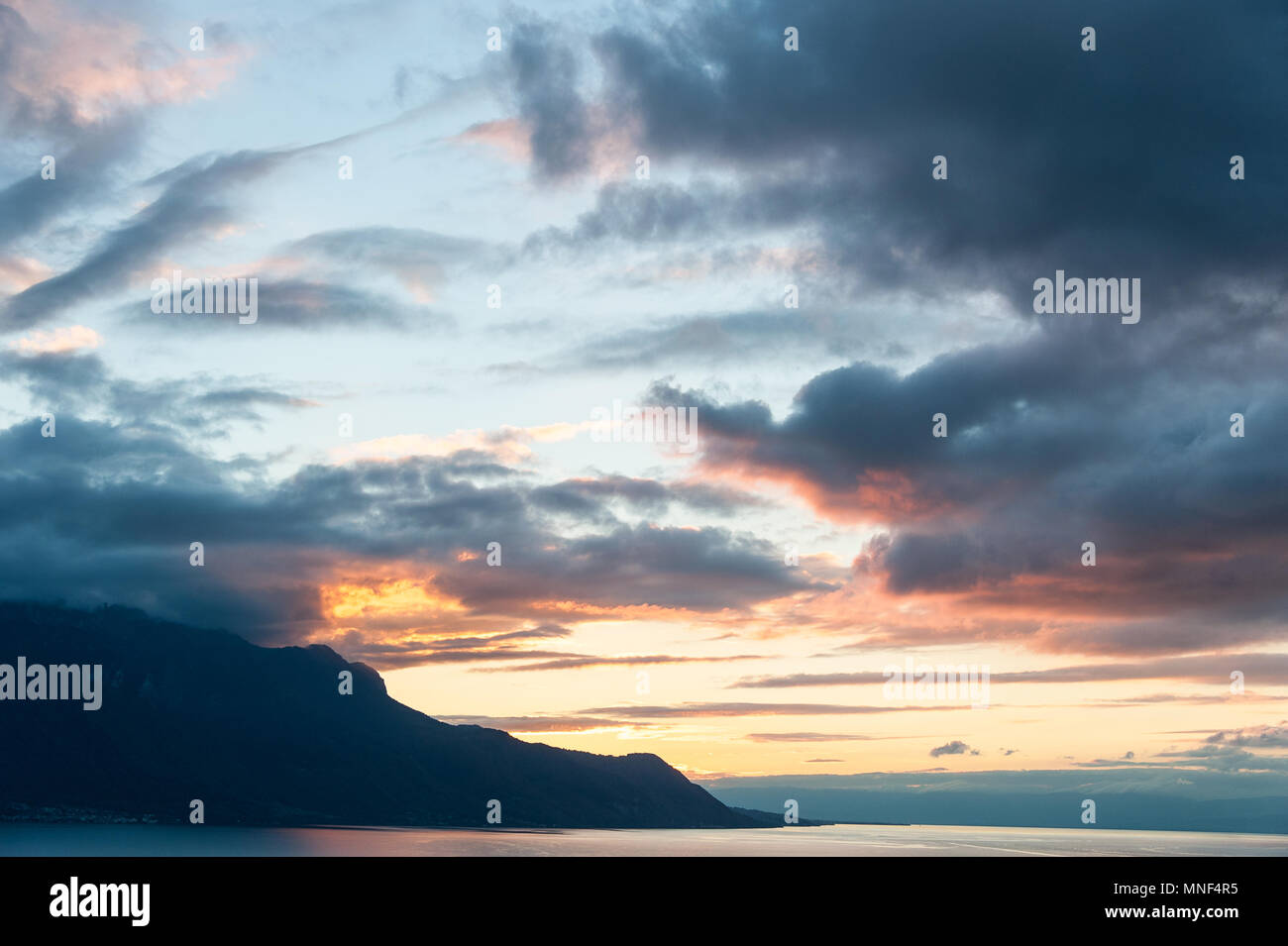 Bel tramonto sul Lago di Ginevra, Svizzera. La luce del sole riflessa sull'acqua, cielo drammatico in un panorama alpino. Foto Stock