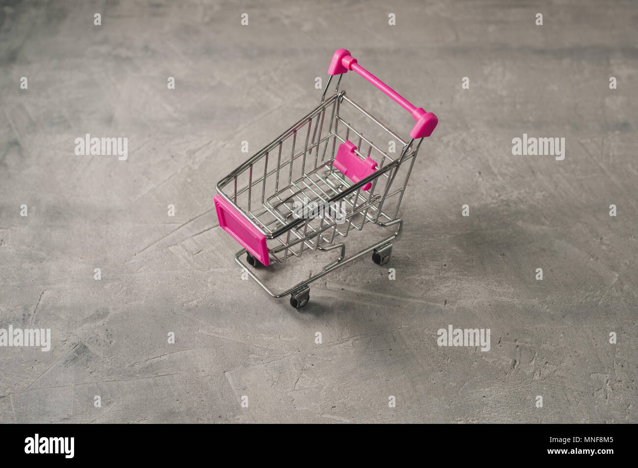 Miniatura rosa vuoto carrello della spesa sul cemento grigio sfondo Foto Stock