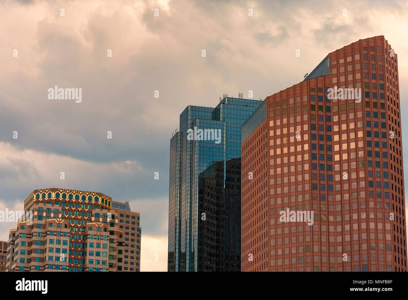 Tre di Boston's skyscrapes glow in the cloud filterd più tardi nel pomeriggio la luce del sole. Foto Stock