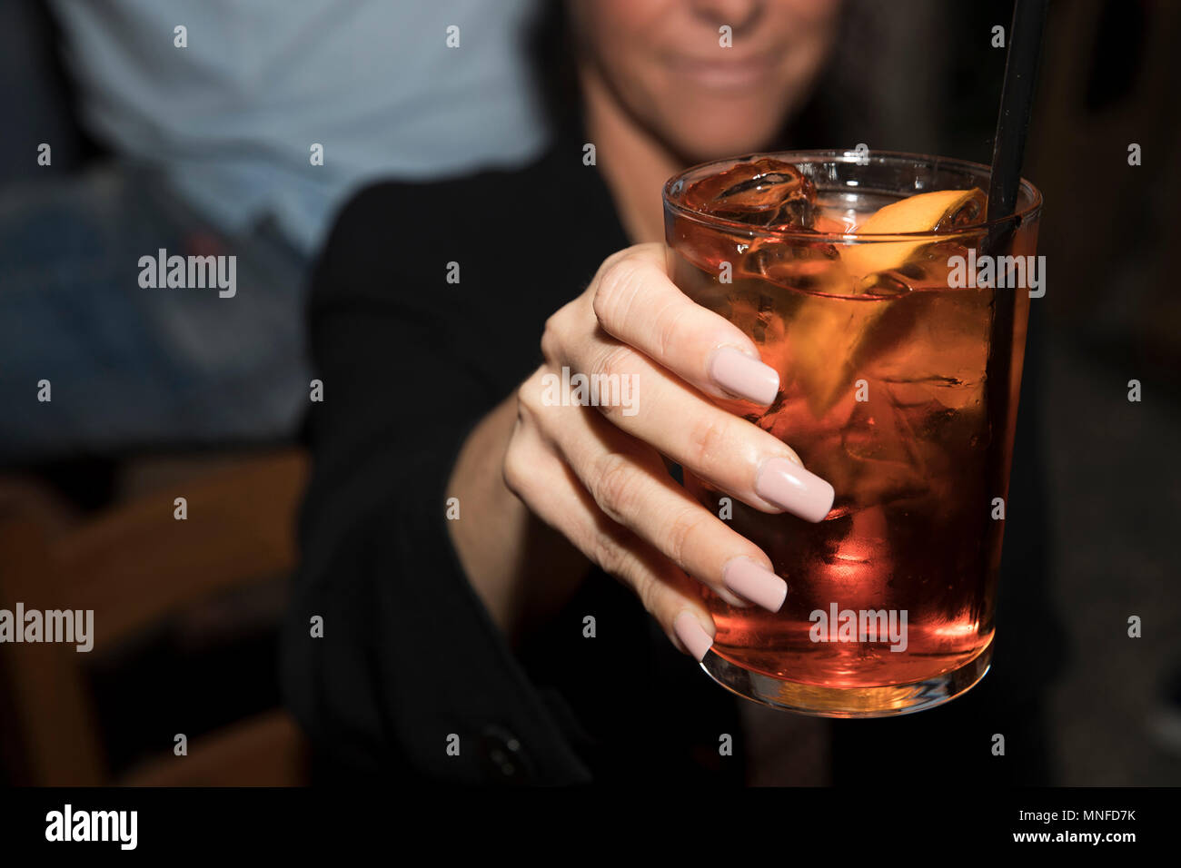 Primo piano di una donna sorridente con lunghi chiodi, tenendo in mano un bicchiere di spritz cocktail verso la telecamera. Foto Stock
