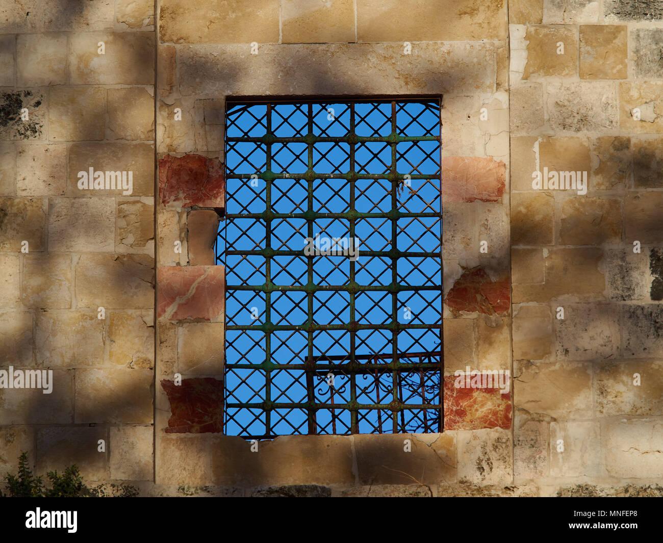 Antica traliccio metallico in uno spesso muro di pietra, attraverso un reticolo è possibile vedere un luminoso cielo blu, Gerusalemme, Israele. Foto Stock