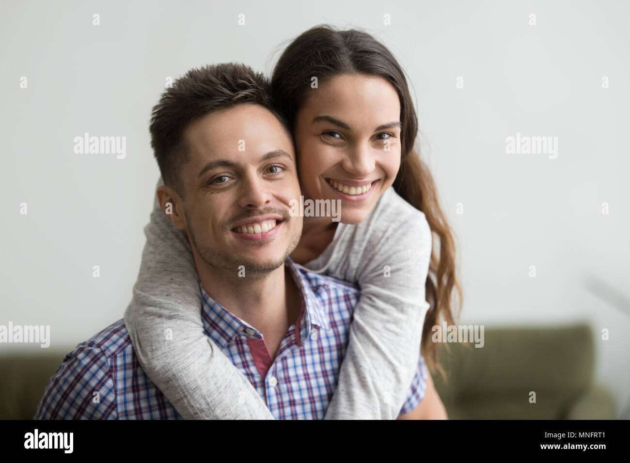 Uomo sorridente piggyback allegro moglie guardando la fotocamera Foto Stock