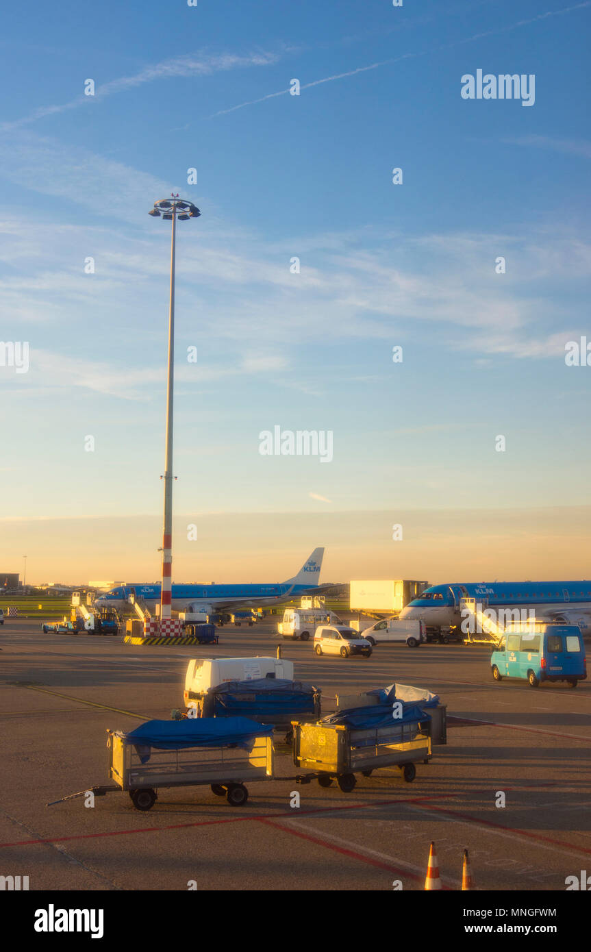 Il piazzale dell'aeroporto internazionale Schiphol di Amsterdam, in Olanda, mostrando aeromobili e carrelli bagagli. Fotografato al tramonto da un piano. Foto Stock