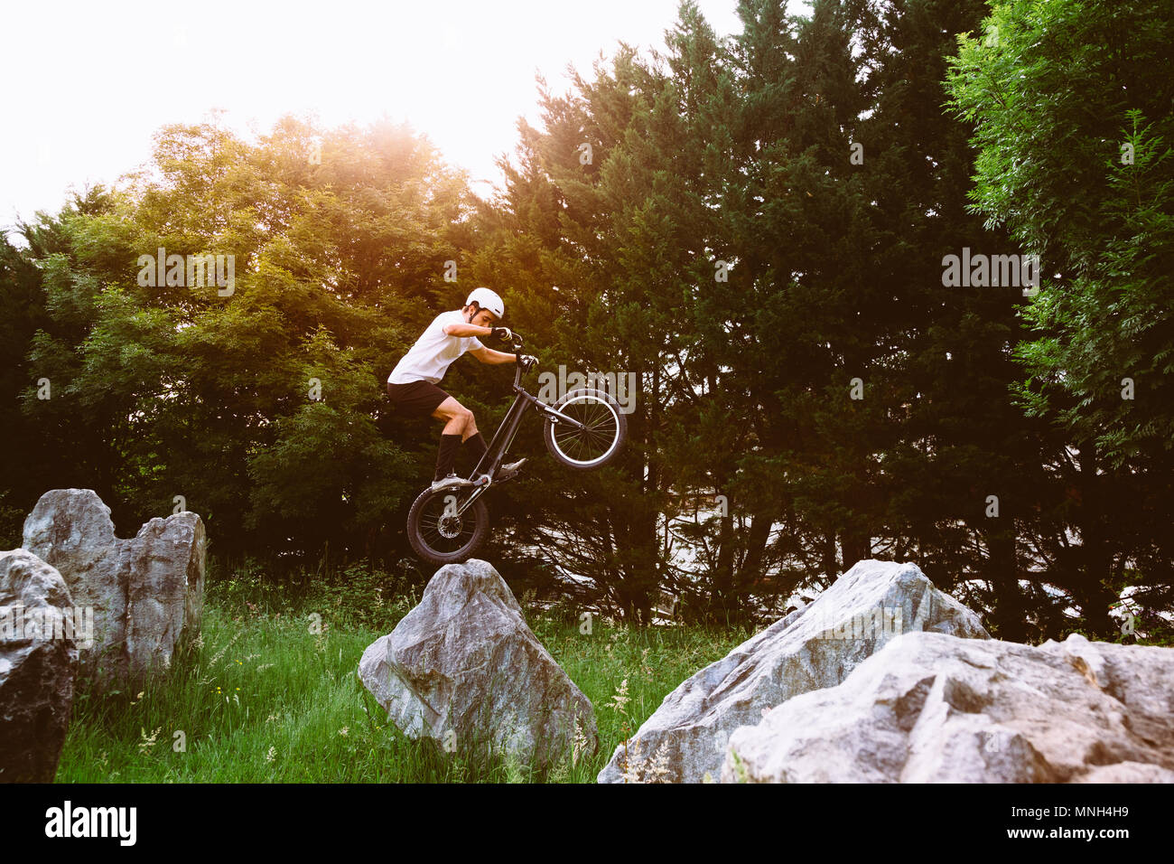 Giovane ciclista jumping con la ruota posteriore di una bicicletta di prova su una roccia al tramonto. Foto Stock