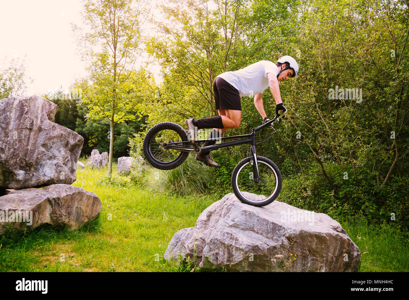 Giovane ciclista jumping con la ruota anteriore di una bicicletta di prova su una roccia Foto Stock