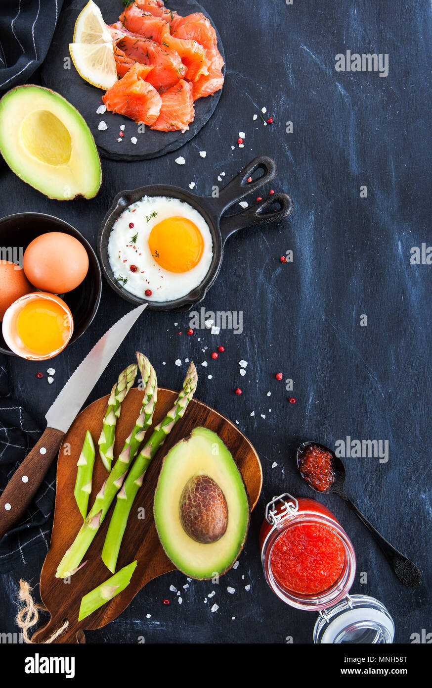 Vista superiore del tavolo per la colazione con uova fritte, avocado, asparagi, caviale rosso e salmone affumicato, spazio di copia Foto Stock