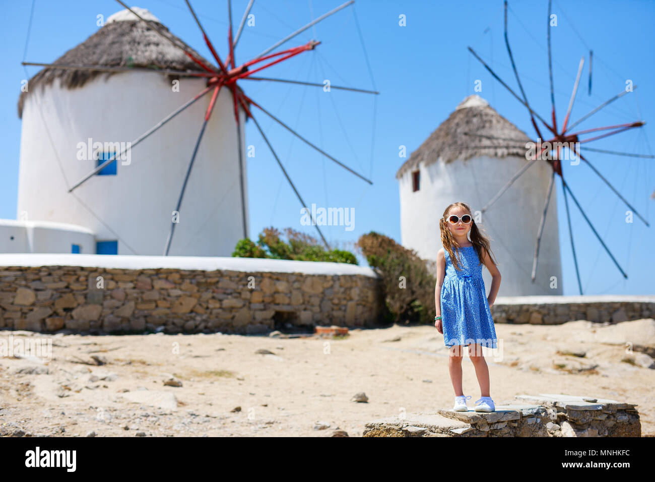 Incantevole piccola ragazza di fronte di mulini a vento in una popolare località turistica sull'isola di Mykonos, Grecia Foto Stock