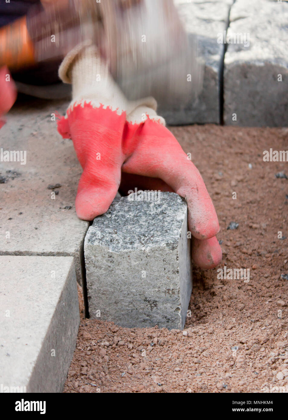 Le mani nei guanti di un lavoratore builder posa sul granito imp ciottoli sulla sabbia con un mazzuolo di gomma martello , e pavimentazione marciapiede di strada su strada con Foto Stock
