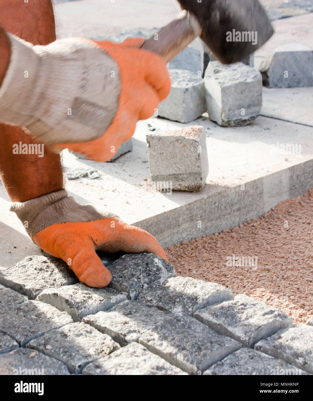 Le mani nei guanti di un lavoratore builder posa sul granito imp ciottoli sulla sabbia con un mazzuolo di gomma martello , e pavimentazione marciapiede di strada su strada con Foto Stock