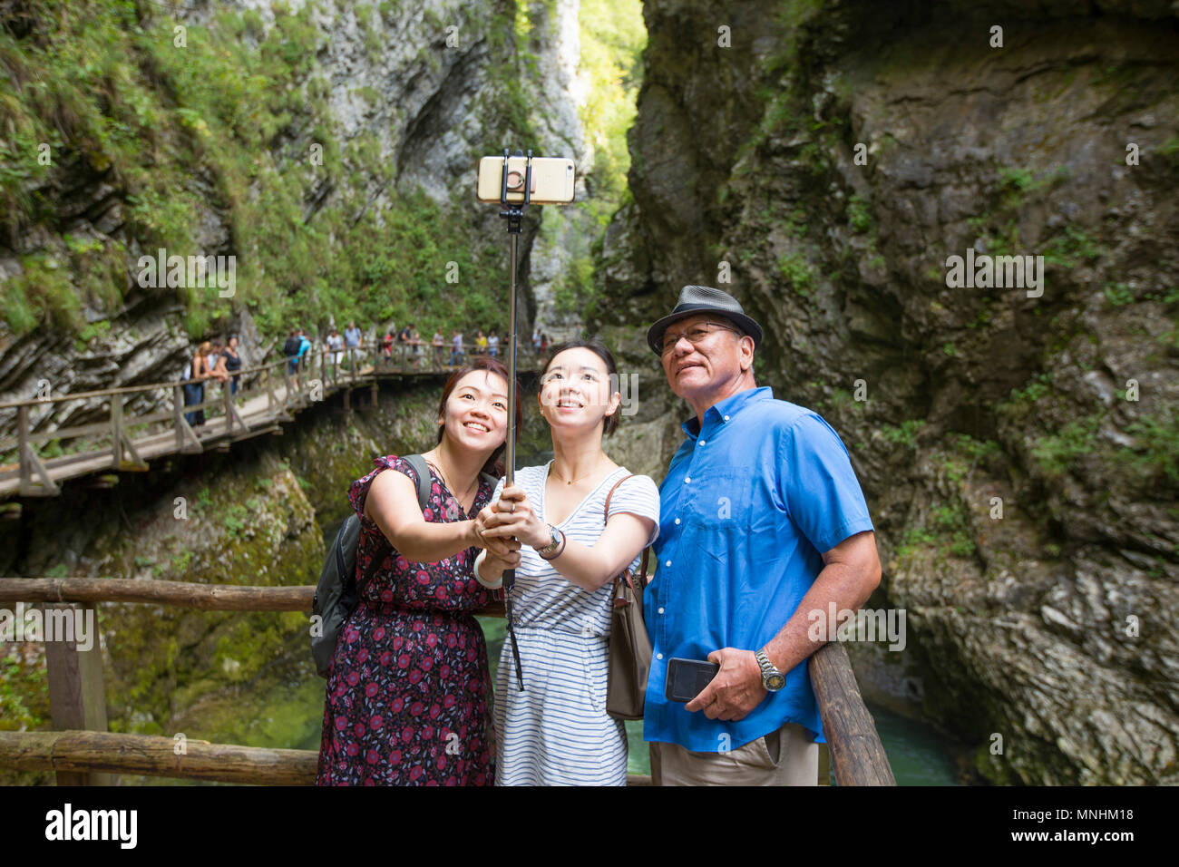Turisti asiatici stanno prendendo un gruppo selfie con uno smart phone su un bastone selfie in gola gorge, Slovenia. La gola gorge è un burrone nelle immedia Foto Stock