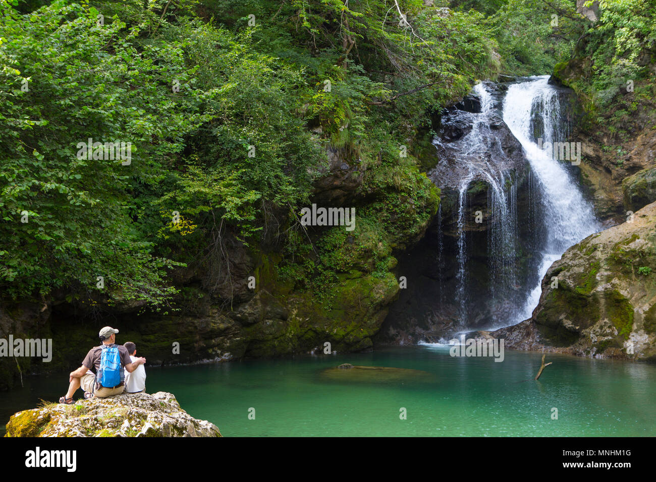 Padre e figlio sono seduti ad una roccia e guardare la famosa cascata di Somma in gola gorge, Slovenia. La gola gorge è un burrone nelle immediate v Foto Stock