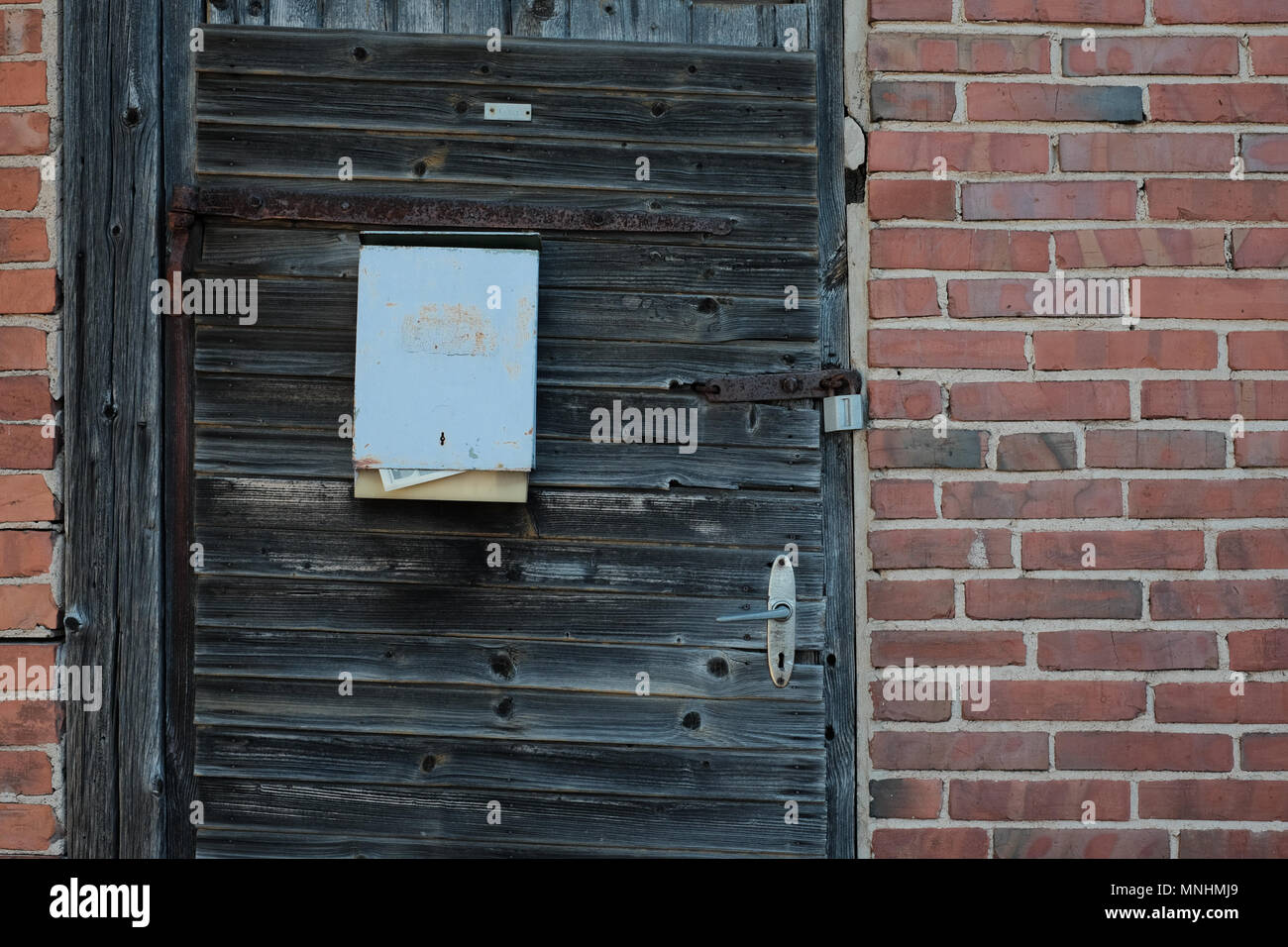 Una vecchia casella con vecchi giornali appesi ad un decadimento della porta di legno di un abbandonato casa di mattoni Foto Stock