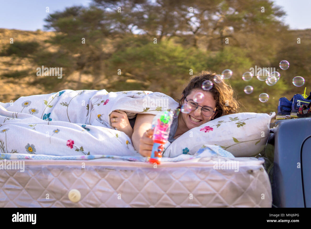 Donna con un sorriso concentraited giocando con il round soap-bolle nel letto matrimoniale,costruita su un pick up truck mentre viaggia all'aperto.con una struttura ad albero blury sfondo Foto Stock