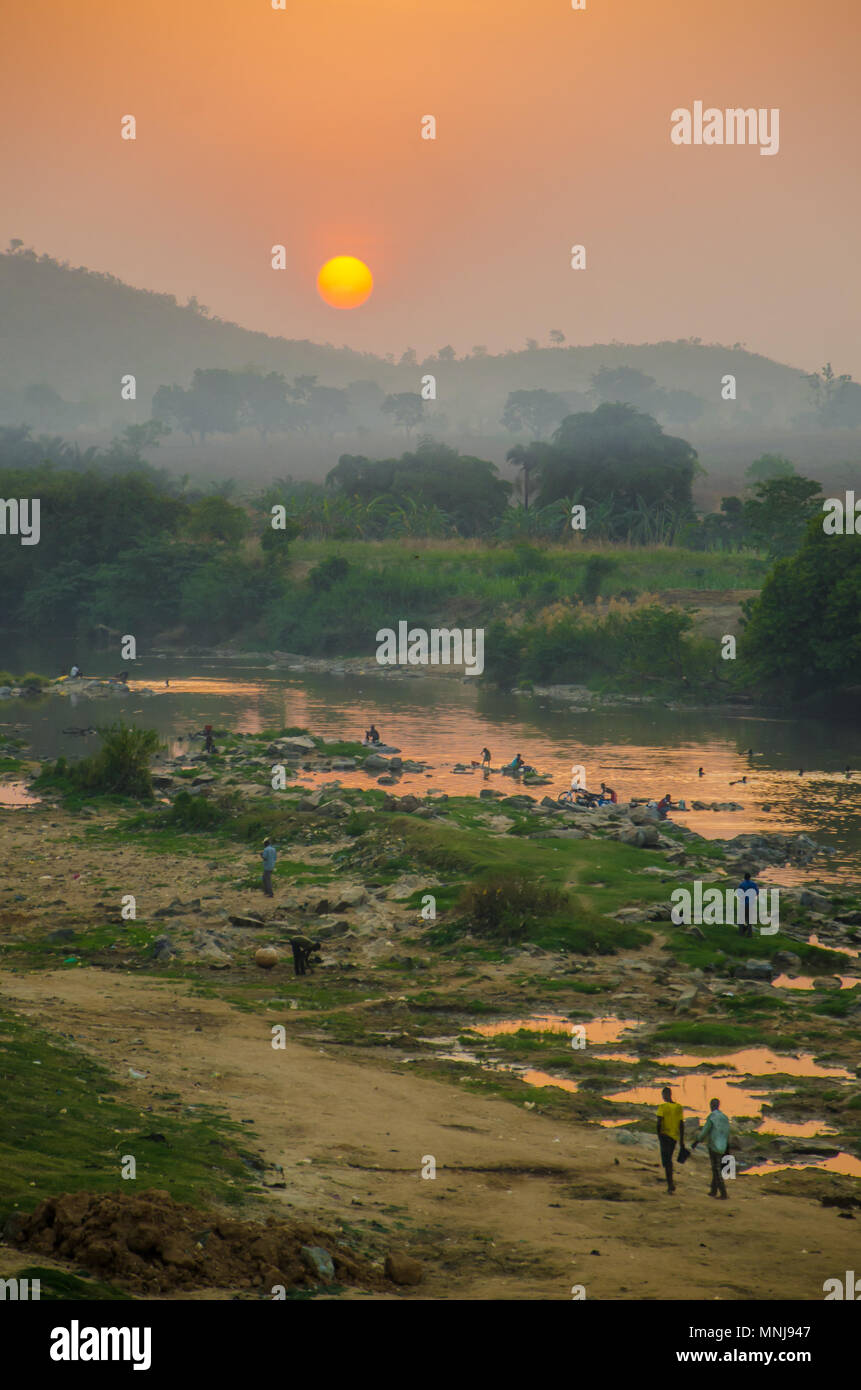 La nebbia rosso tramonto sul fiume con il popolo africano a piedi e lavaggio, Nigeria, Africa Foto Stock