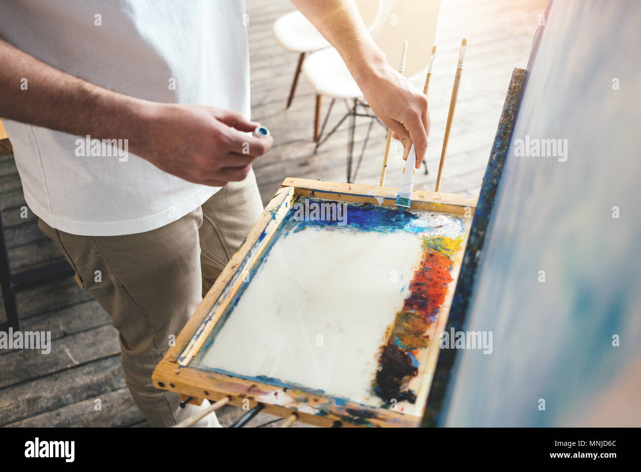 Pittore olio mix di colori di vernice sulla tavolozza in officina. Gli uomini artista luce in studio. Lente effetto flare Foto Stock