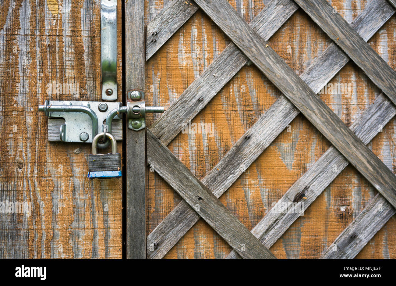 La vecchia porta di legno con diagonale square scolorito martellato listelli sottili è chiuso sul fermo di metallo e un lucchetto per la memorizzazione sicura di articoli per la casa Foto Stock