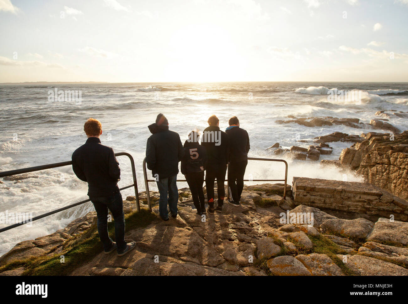 Un gruppo di persone in piedi a costa e ammirando scenic la vista del tramonto sul mare, Ploemeur, Morbihan, Francia Foto Stock