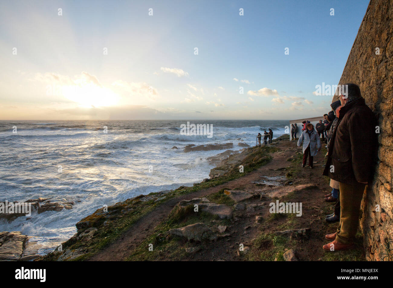 Un gruppo di persone in piedi lungo la parete costiere e ammirando scenic la vista del tramonto sul mare, Ploemeur, Morbihan, Francia Foto Stock