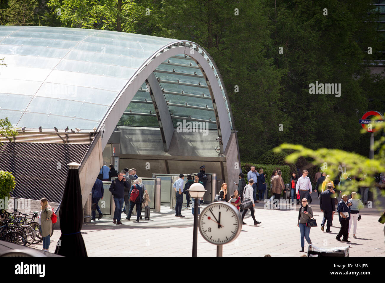 Stazione metropolitana di Canary Wharf entrata nel sole di primavera, con un orologio in primo piano Foto Stock
