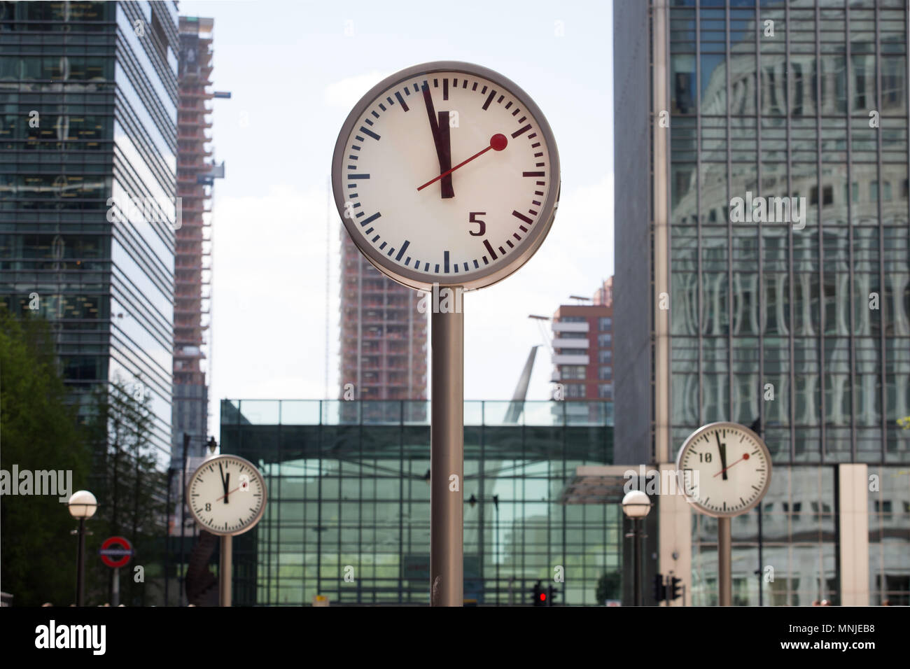 Canary Wharf, orologi visualizza il tempo appena prima delle 12pm al di fuori della stazione della metropolitana con i dipendenti fresatura intorno godendosi il sole Foto Stock