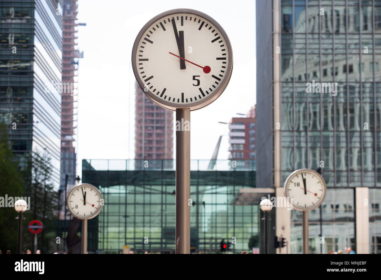 Canary Wharf, orologi visualizza il tempo appena prima delle 12pm al di fuori della stazione della metropolitana con i dipendenti fresatura intorno godendosi il sole Foto Stock