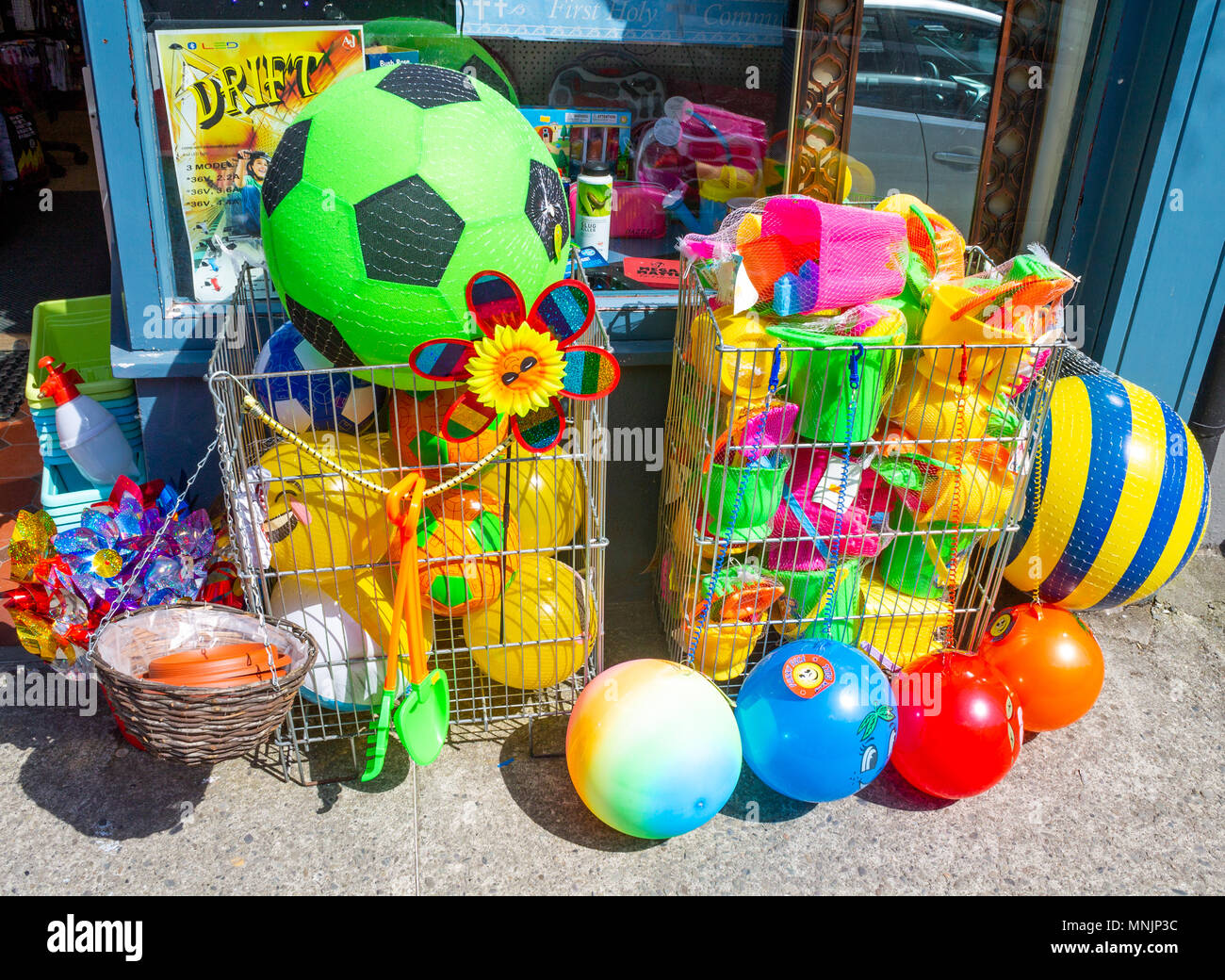 Vivacemente colorato o di colore palle da spiaggia in vendita sul marciapiede o sentiero al di fuori di un negozio, con secchio di plastica e vanga. Foto Stock