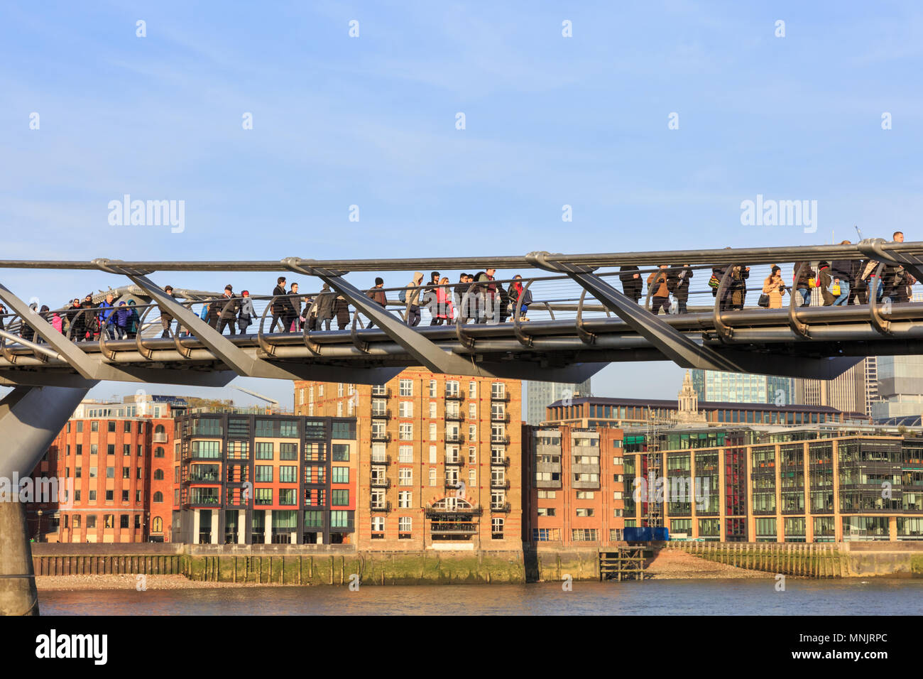 La gente camminare attraverso il Millennium Bridge sopra il fiume Tamigi in una bella giornata di sole, London, England, Regno Unito Foto Stock