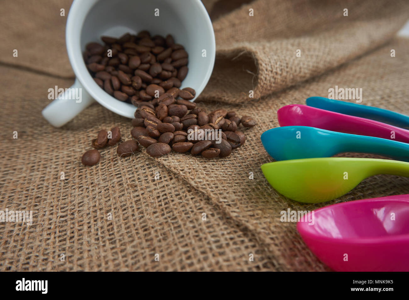 Allentate il caffè torrefatto in grani, porcellana bianca tazza da caffè e plastica di colore dose Misurini sul sacco di iuta. Concettuale della quantità consigliata di caffè Foto Stock