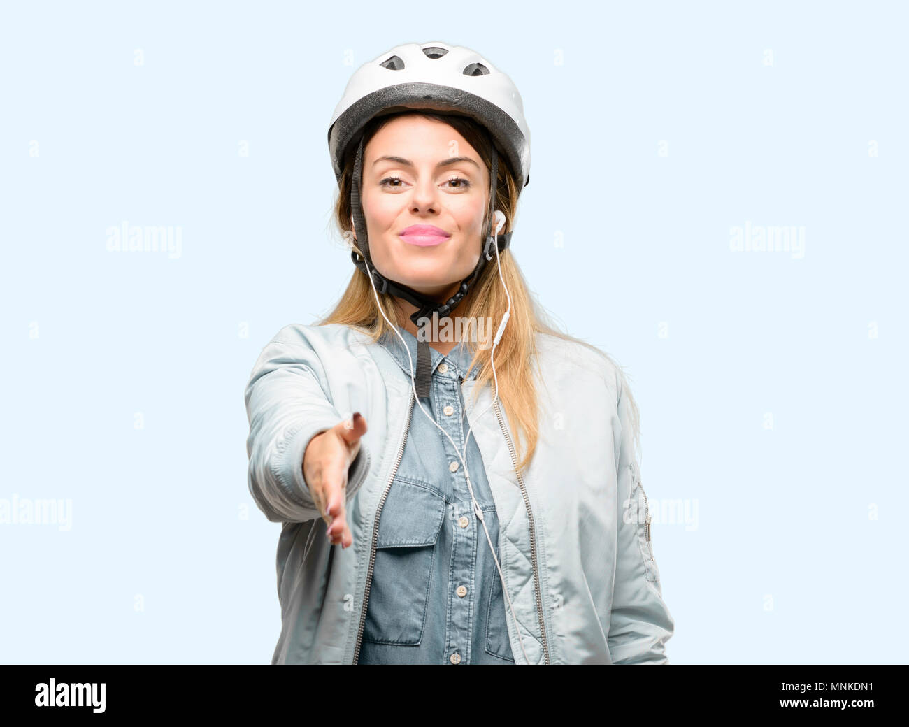 Giovane donna con il casco protettivo e auricolari tiene per mano accogliente nella posa di handshake, esprimendo la fiducia e il concetto di successo, saluto Foto Stock