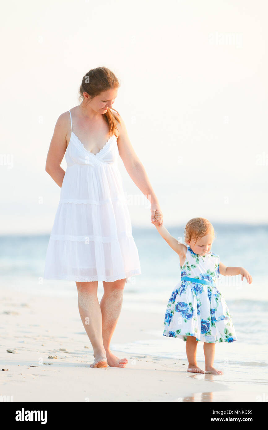 Foto verticale della giovane madre e la sua adorabile bambina sulla spiaggia al tramonto Foto Stock