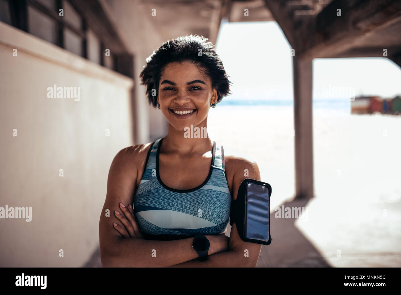 Ritratto di donna fitness all'aperto permanente e sorridente. Atleta femminile prendendo una pausa dopo la sessione di allenamento. Foto Stock