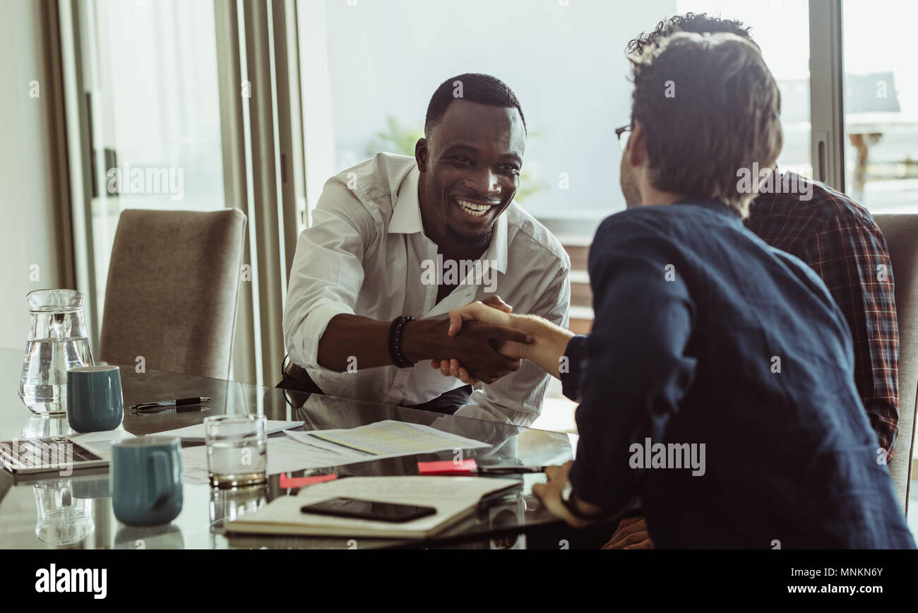 Discutere gli imprenditori lavorano seduti ad un tavolo per conferenza in ufficio. Gli uomini si stringono la mano e sorridente durante una riunione di affari. Foto Stock