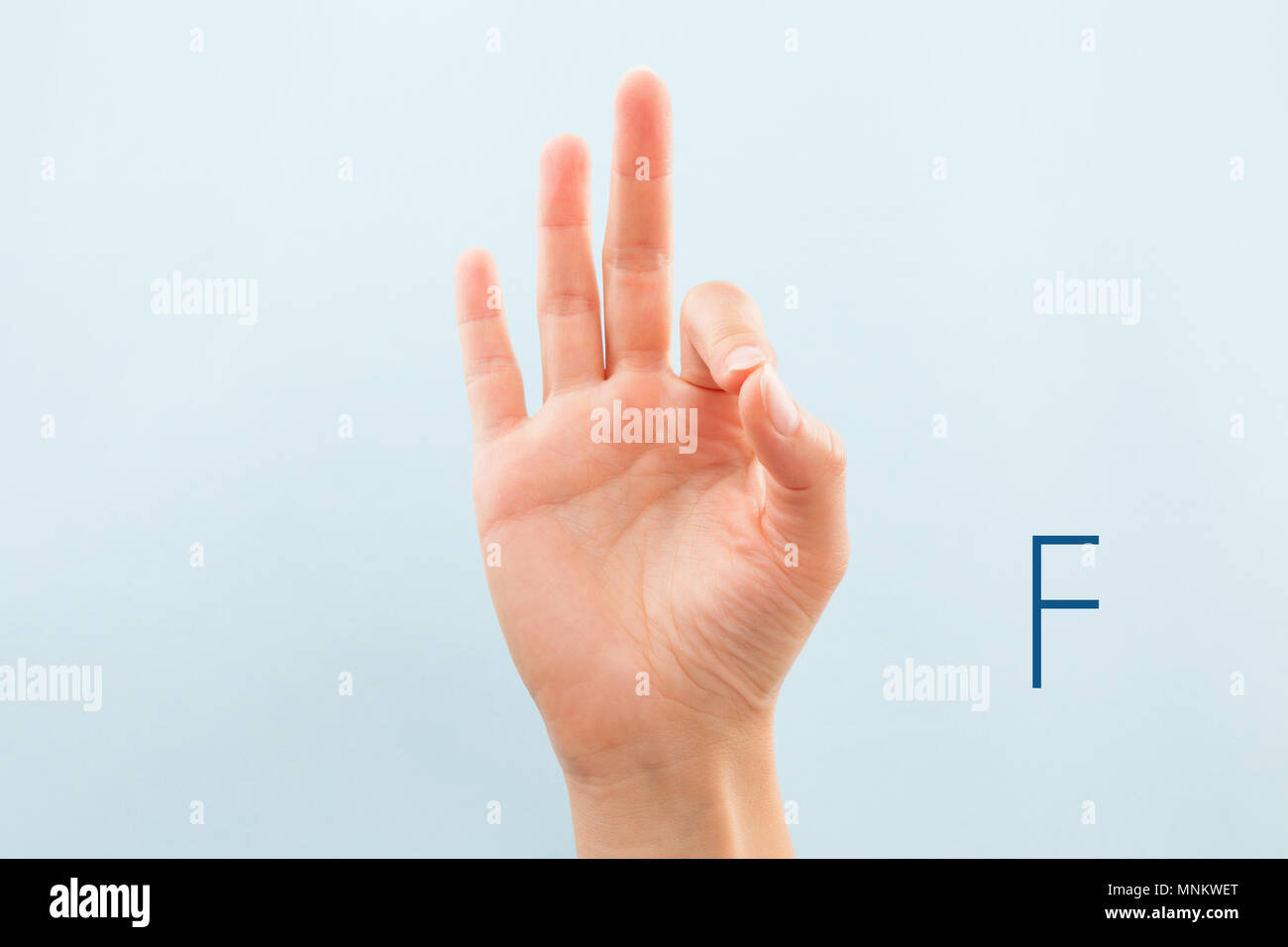 American Sign Language. Mano femminile che mostra la lettera F isolato su sfondo blu. Foto Stock