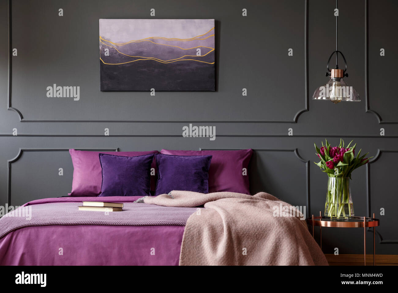 Un lenzuolo sul letto viola accanto al tavolo con fiori in camera da letto interno con poster sul muro grigio Foto Stock