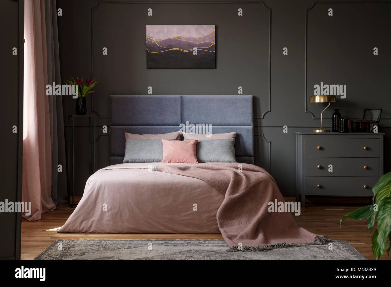 Lampada oro su cabinet grigio accanto al letto in camera da letto pastello interni con pittura viola Foto Stock