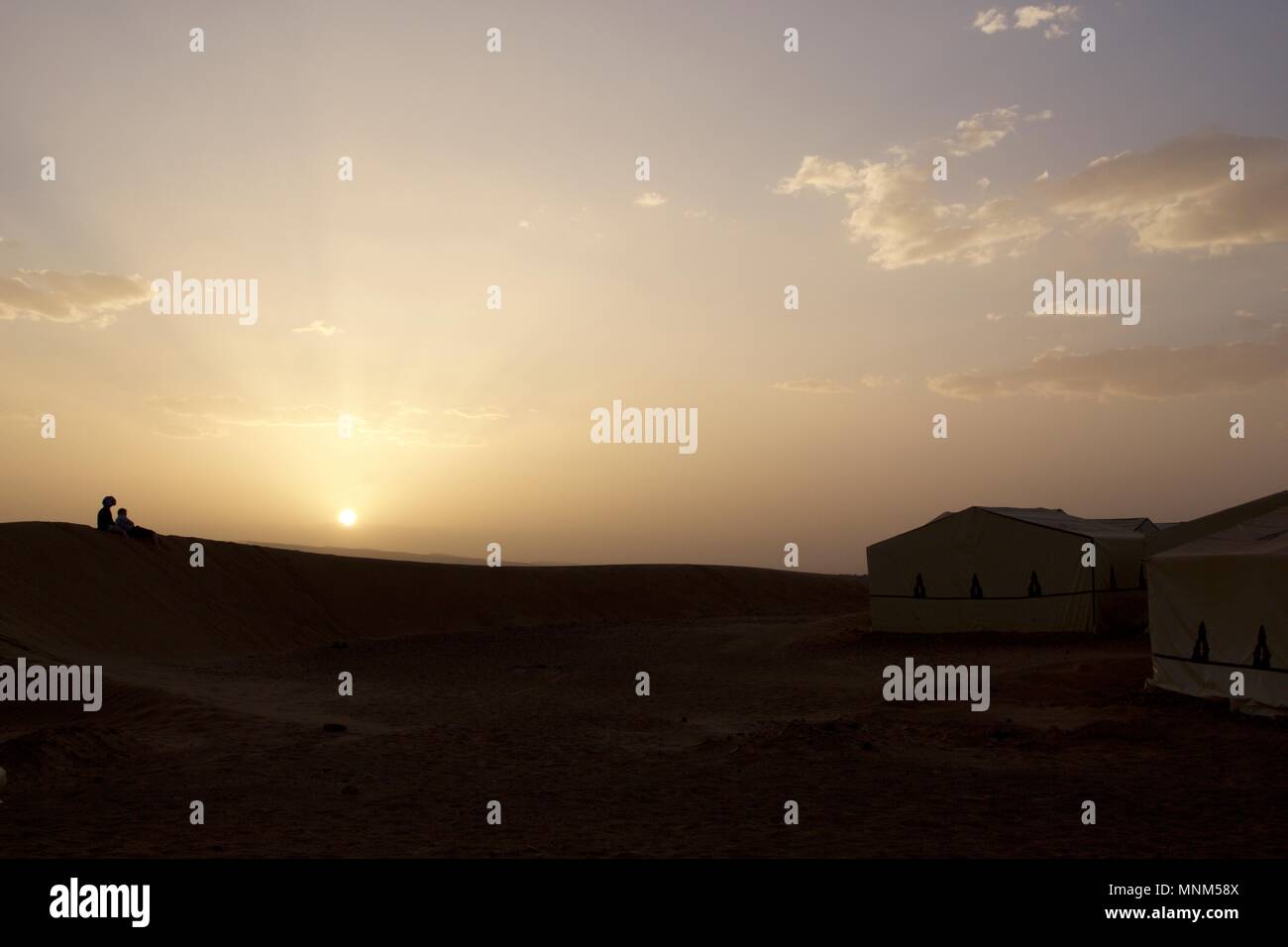 Un giovane seduto su di una duna di sabbia e guardare il tramonto sopra il deserto Zagora, Marocco Foto Stock