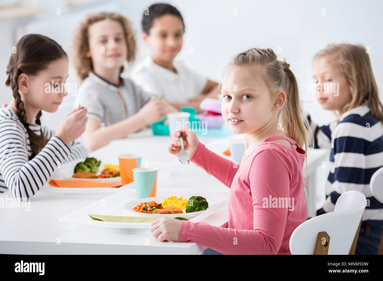 Ragazza di mangiare le verdure con amici in mensa durante la pausa a scuola Foto Stock