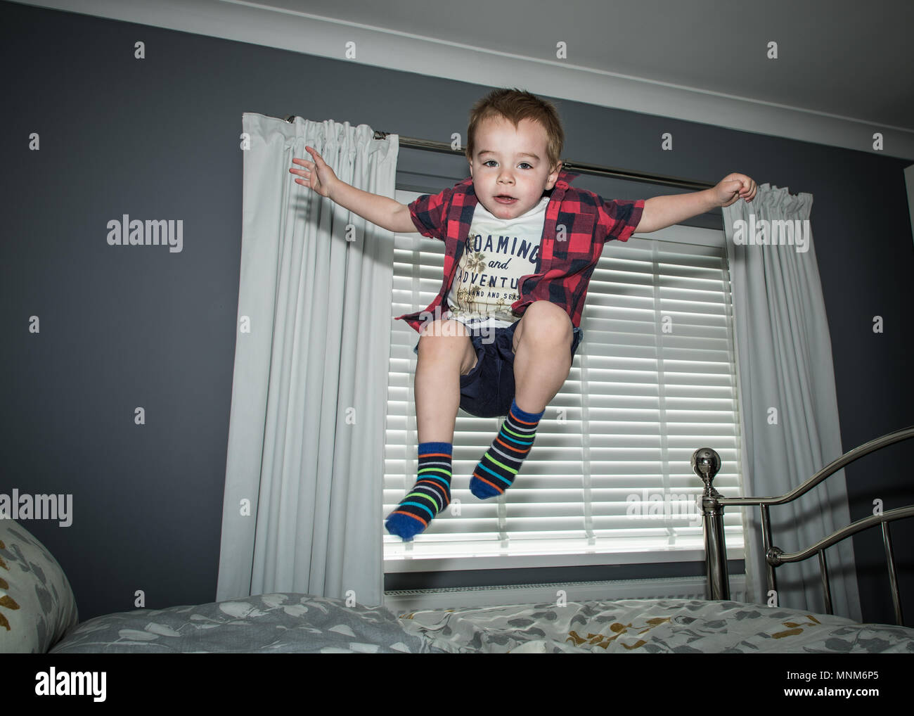 Un ragazzino salta su un letto in una camera da letto / Bambino saltando sul letto Foto Stock