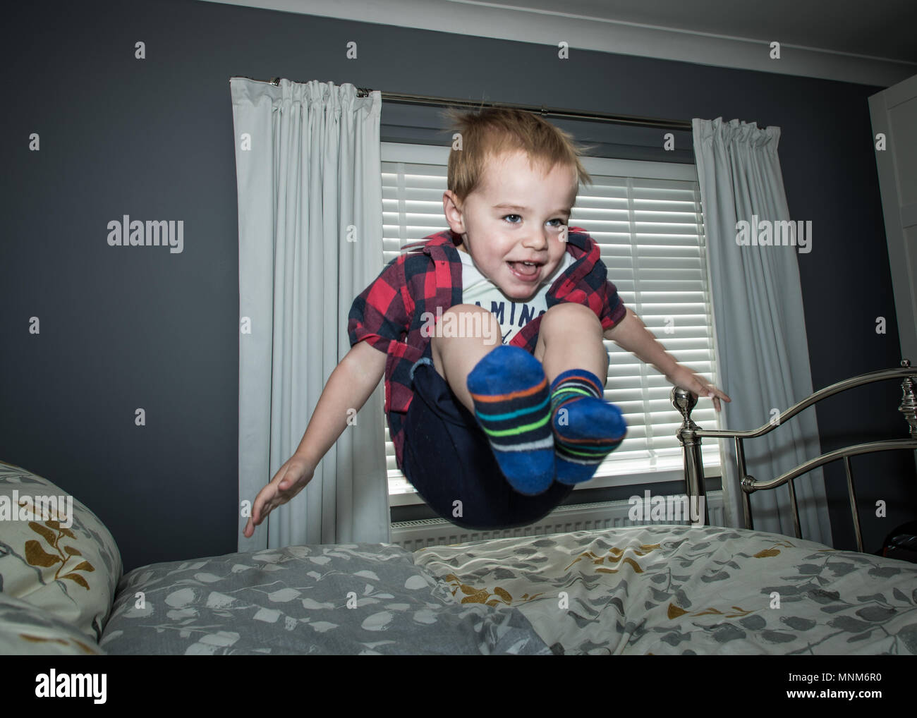 Un ragazzino salta su un letto in una camera da letto / Bambino saltando sul letto Foto Stock