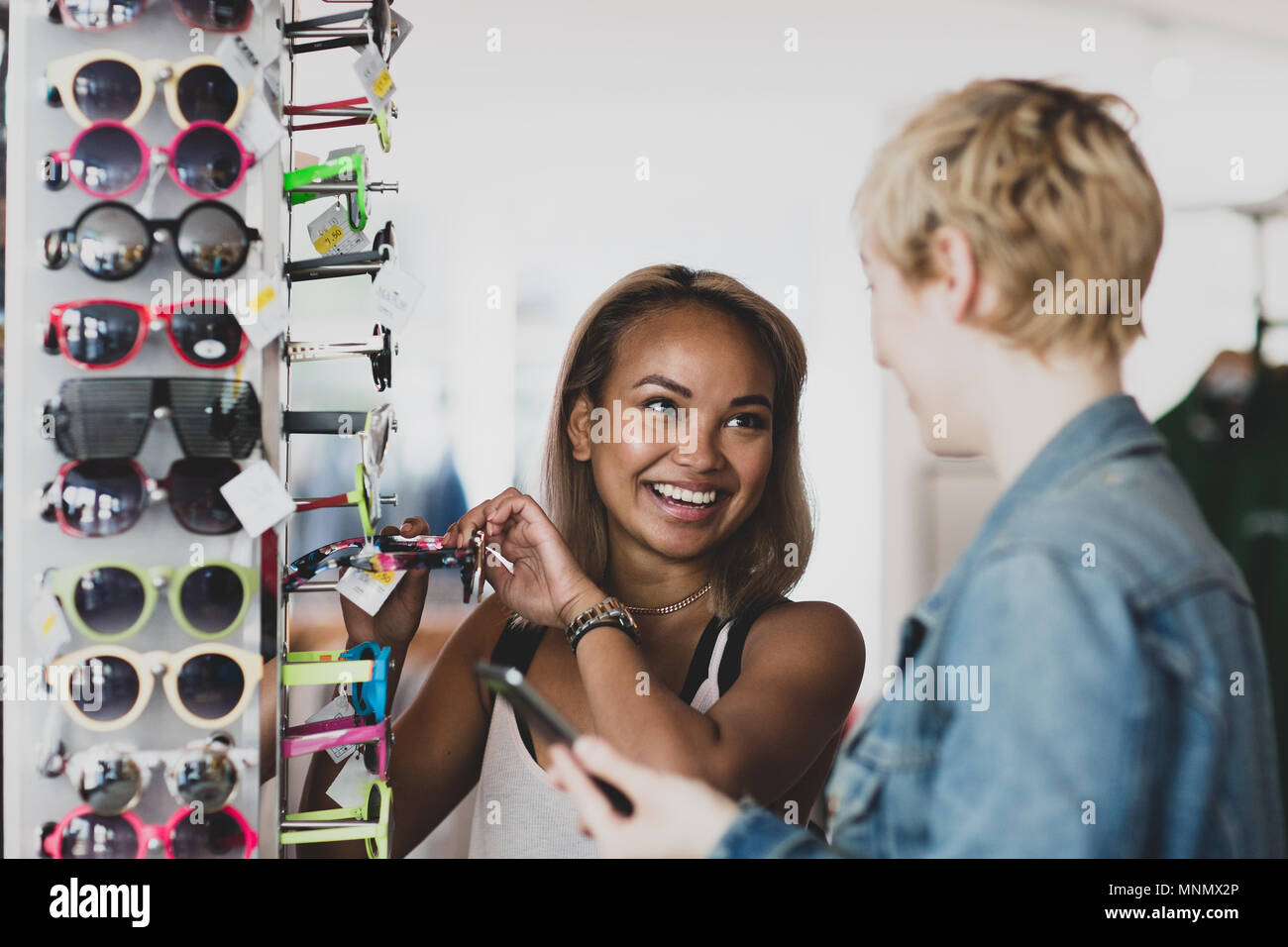 Millennial cercando su occhiali da sole in un negozio vintage Foto Stock
