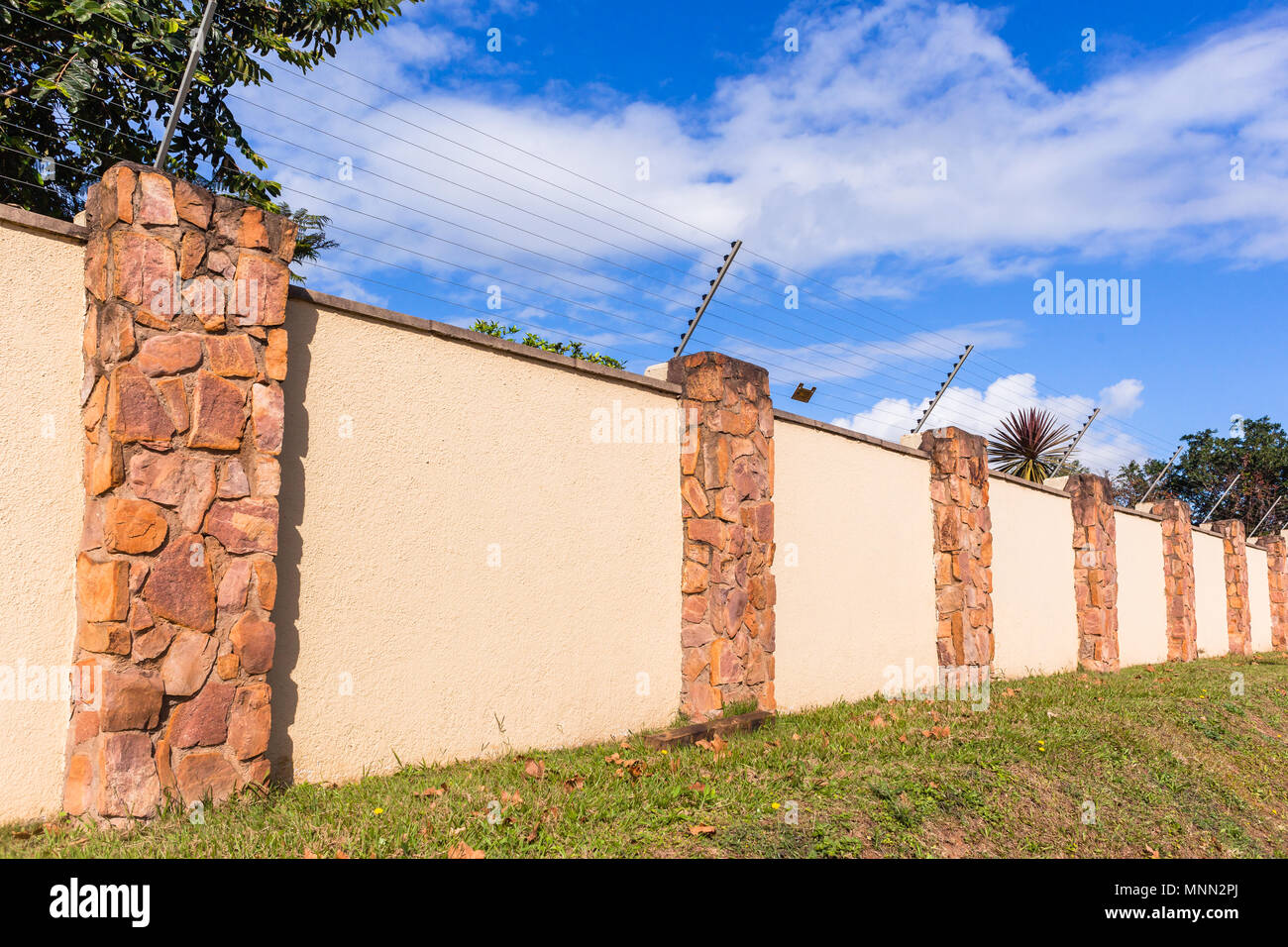 Elettrificate recinto di filo sul lungo muro di cinta della sicurezza per cancelli di proprietà residenziale. Foto Stock