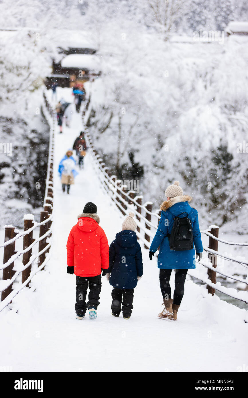 La famiglia di madre e bambini attraversando il ponte sul fiume Shogawa nello storico villaggio giapponese Shirakawa-go in inverno Foto Stock