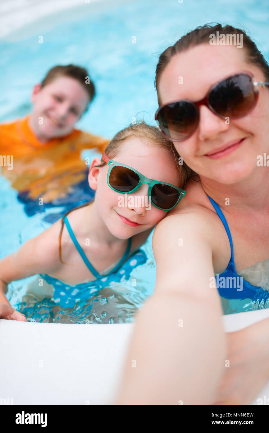 Felice madre e i suoi bambini in piscina all'aperto tenuto selfie sulla vacanza tropicale Foto Stock