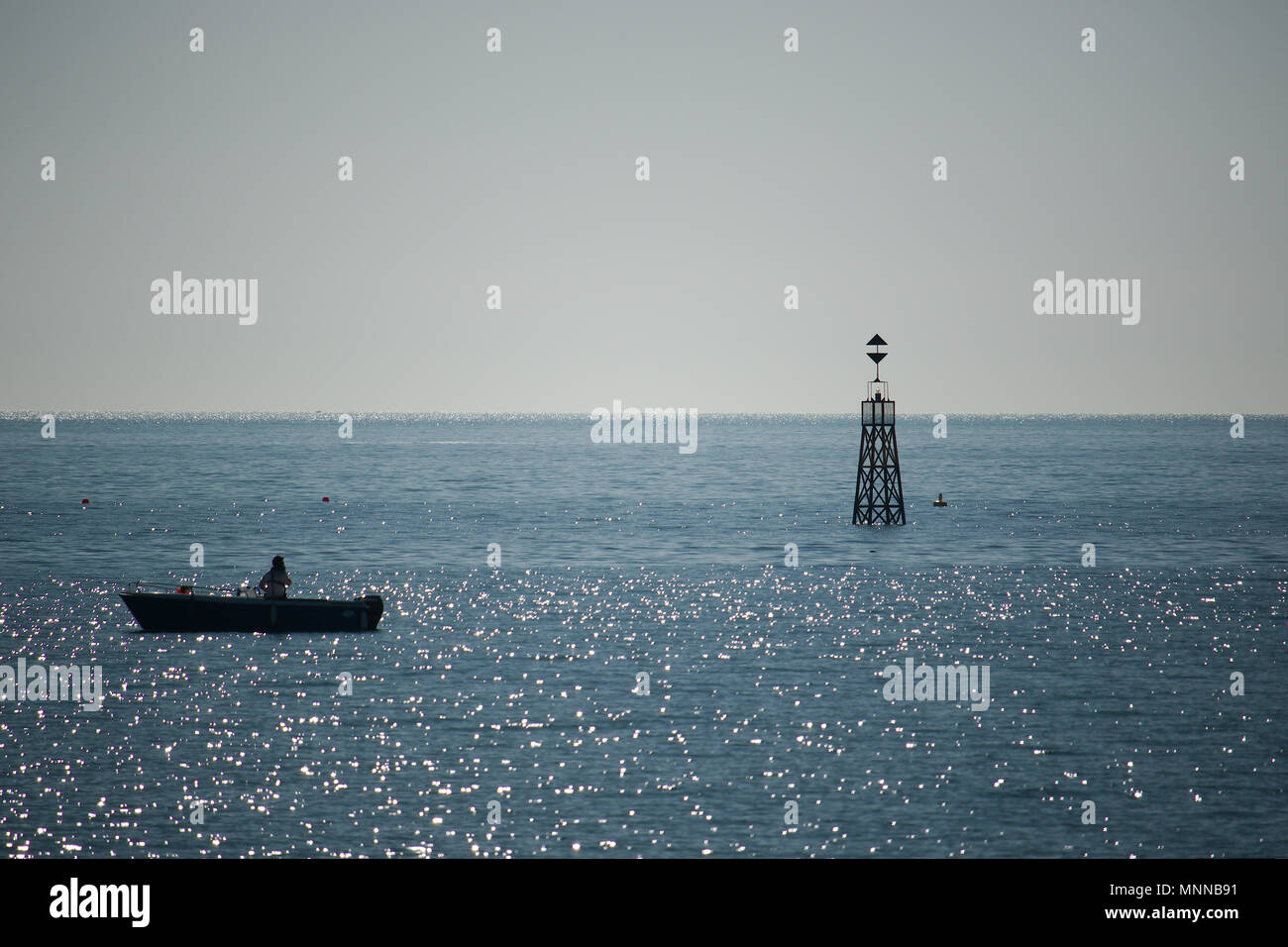 Una visione minimalista di un mare calmo e cielo chiaro con una sola barca a remi e torre di avvistamento in vista. Foto Stock