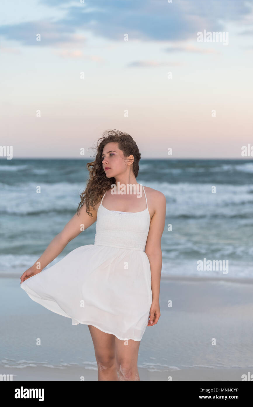 Giovane donna in abito bianco sul tramonto sulla spiaggia in Florida  Panhandle con il vento e le onde del mare, profilo laterale che guarda  lontano Foto stock - Alamy