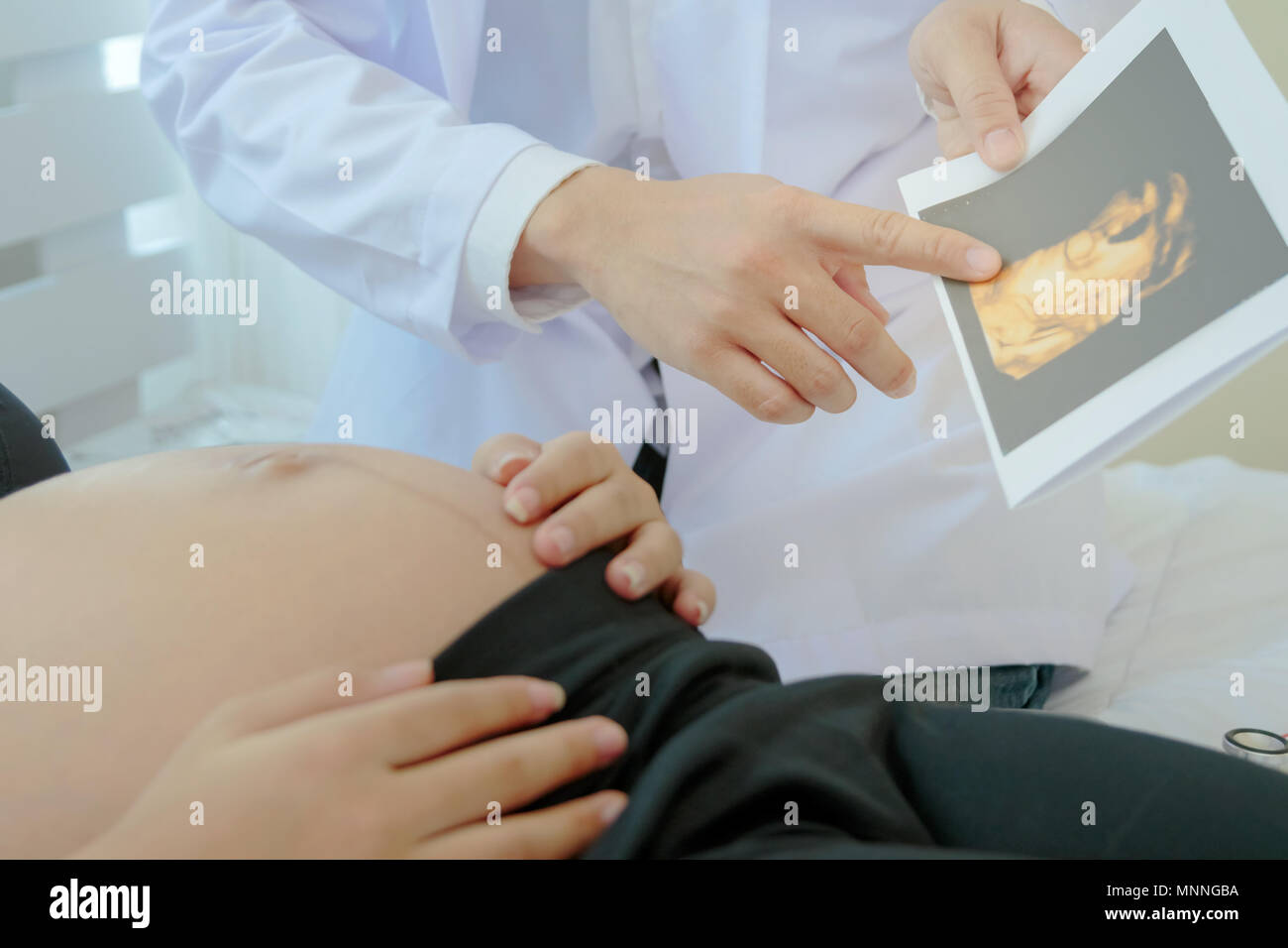 La donna incinta è sdraiato sul letto mentre il medico che mostra l'immagine ad ultrasuoni. Foto Stock
