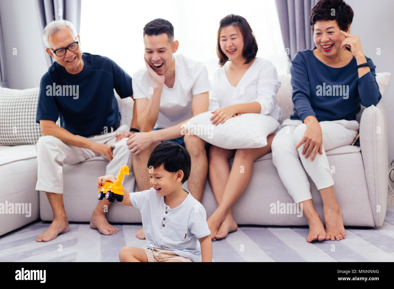 Felice Asian estesa famiglia seduti sul divano insieme e guardare i bambini giocare giocattolo sul pavimento con la felicità Foto Stock