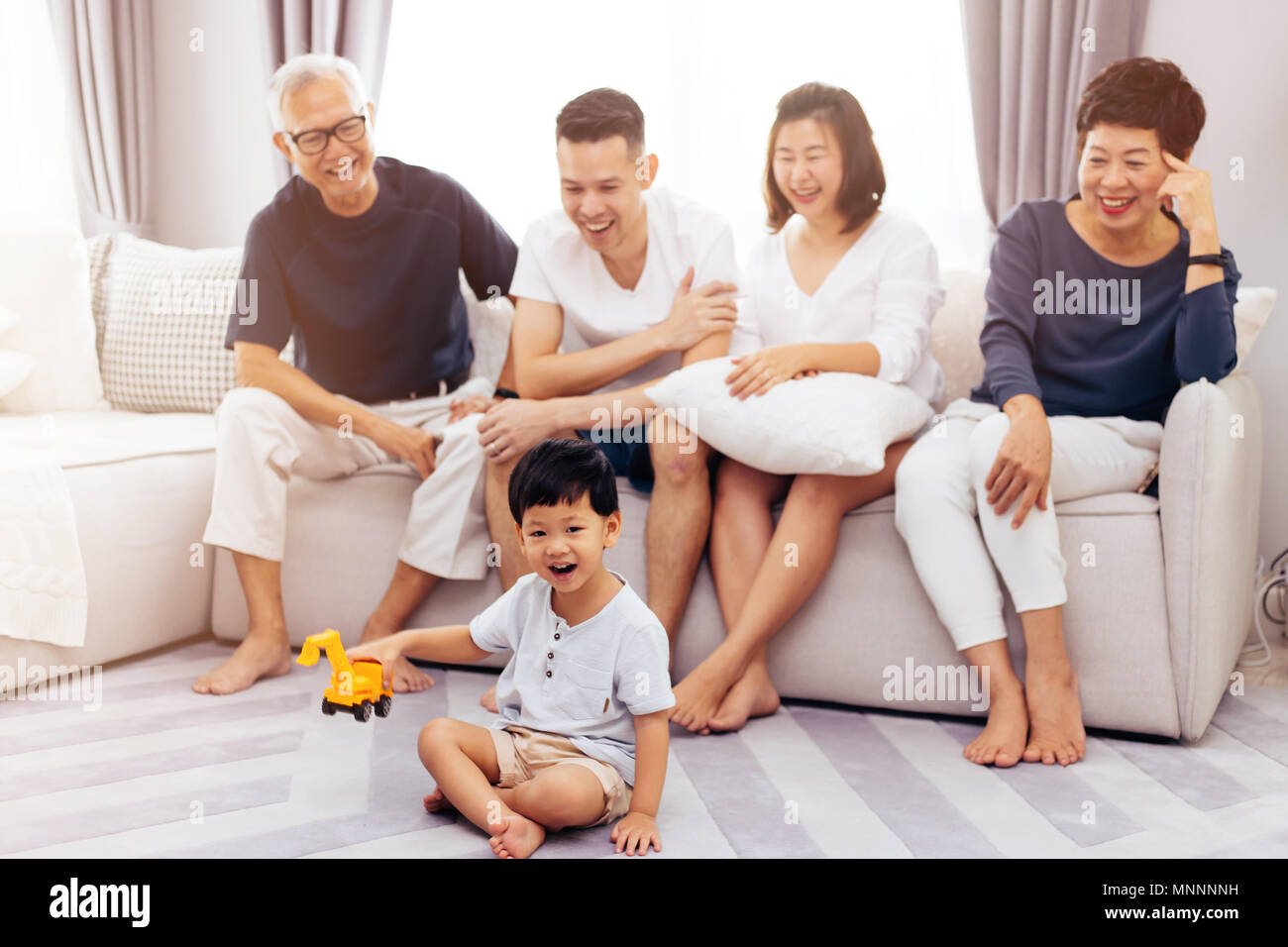 Felice Asian estesa famiglia seduti sul divano insieme e guardare i bambini giocare giocattolo sul pavimento con la felicità Foto Stock
